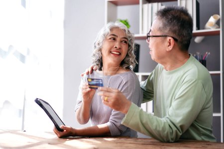 Foto de Pareja mayor tiene tarjeta de crédito y tableta digital para comprar seguro de vida y compras en línea, mientras que pasar tiempo para hacer actividad para la relajación en la jubilación de vida juntos en la sala de estar del hogar. - Imagen libre de derechos