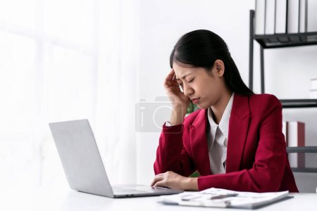 Photo for Businesswoman in suit stressful and headache while thoughtful about accounting of new business and typing information with keyboard on laptop during working on the table in modern workspace. - Royalty Free Image