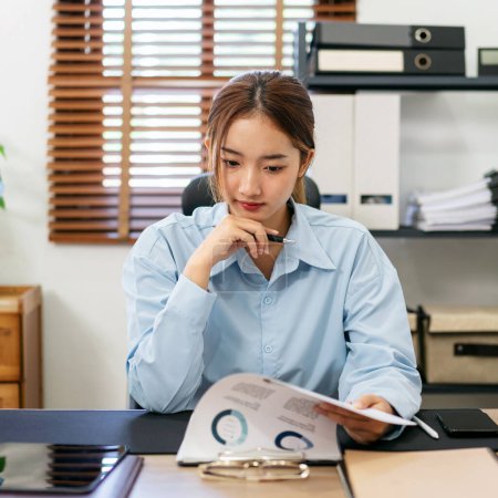 Photo for Businesswoman is thoughtful about accounting of business while reading information of new business project in document and working on laptop at modern office. - Royalty Free Image