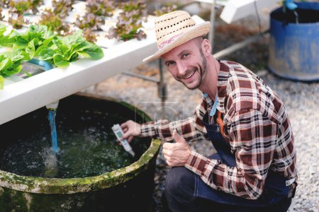 Téléchargez les photos : Exploitant agroalimentaire et concept d'agriculture hydroponique, Homme utilisant le pH-mètre pour tester et contrôler le système d'eau de la ferme hydroponique pour la plantation de légumes-salades en serre. - en image libre de droit