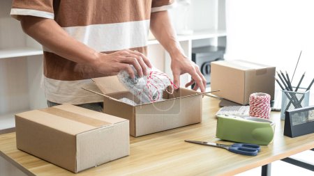 Téléchargez les photos : Homme entrepreneur emballe le produit dans des boîtes en carton pour se préparer à envoyer le client tout en travaillant la livraison d'achats en ligne au bureau à domicile. - en image libre de droit