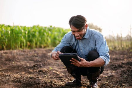 Téléchargez les photos : Fermier intelligent utilisant une tablette numérique pour examiner la qualité du sol pour le contrôle du système de travail et de planification avant la culture de légumes avec la technologie dans le domaine agricole. - en image libre de droit
