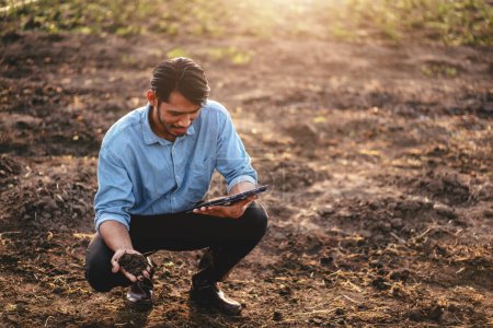 Téléchargez les photos : Fermier intelligent tenant le sol dans sa main et utilisant une tablette numérique pour examiner la qualité du sol pour le contrôle du système de travail et de planification avant la culture de légumes avec la technologie dans le domaine agricole. - en image libre de droit