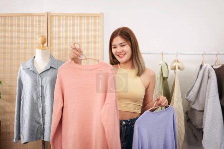 Photo for Woman designer entrepreneur showing clothes product on live online social media streaming and packing into cardboard box to preparing for shipping customer delivery at home. - Royalty Free Image