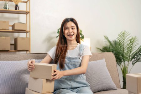 Photo for Young entrepreneur is packing products into cardboard boxes to preparing for home delivery to client while sitting on comfortable the couch and working in living room at home office. - Royalty Free Image