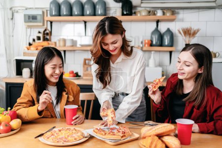 Téléchargez les photos : Groupe d'amis mangeant des pizzas italiennes et buvant des boissons ensemble tout en profitant de la fête pour célébrer le week-end dans la cuisine à la maison. - en image libre de droit