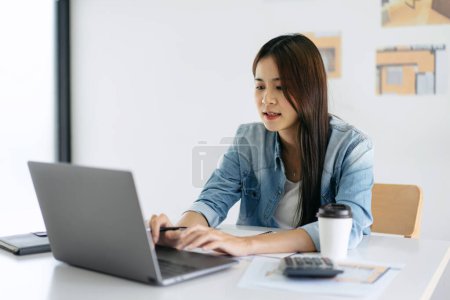 Photo for Woman architect typing data on laptop for sketching and designing building on blueprint while working about planning construction project on laptop in modern office. - Royalty Free Image