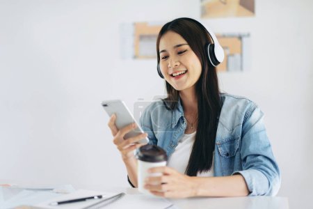 Photo for Woman architect drinking coffee and wearing headphone to listening music while working on laptop about planning construction project on laptop in modern office. - Royalty Free Image
