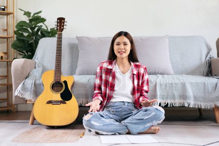 Photo for Young woman is feeling confused while compose the song to writing lyrics on notebook and sitting on the floor in living room at home. - Royalty Free Image