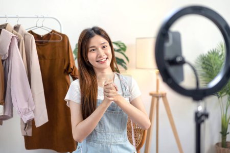 Photo for Female online seller is using smartphone to broadcast live on Vlog for introduce new fashions and talking with customer to selling online clothing on social media. - Royalty Free Image