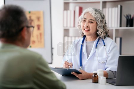 Photo for Female doctor writing prescription on clipboard while explaining medicine use and discussing about healthcare to senior patient after physical his health checkup in hospital. - Royalty Free Image
