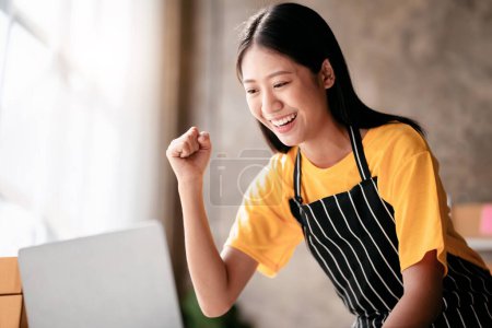 Small business parcel delivery concept, Female entrepreneur checking online order on laptop and raising arm to celebrate for work successfully while working about shopping online sales business.