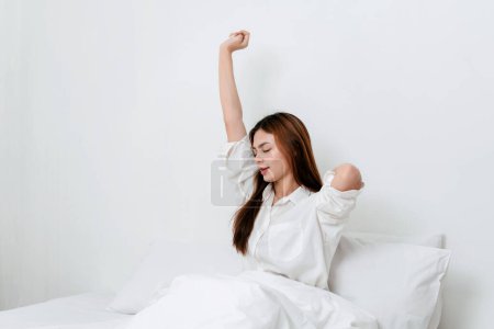 Activity at home leisure lifestyle concept, Young woman in clothes casual raising arms to stretching for relax after wake up in morning while sitting on comfy bed to leisure with lifestyle at home.