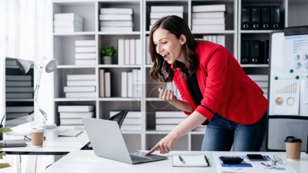 Accounting business concept, Accountant woman using laptop with excited and raising fist to celebrate achievement while working to typing about investment with business planning finance.