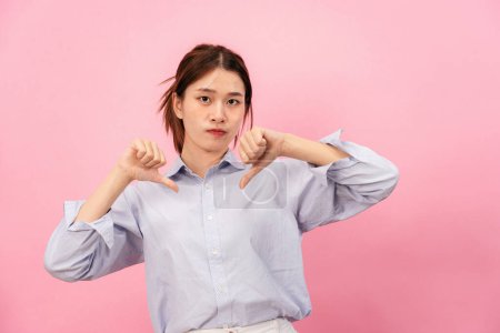 Photo for Young asian woman using hands and fingers while showing thumbs down for symbol of dislike or unlike with disappointed face isolated over pink background. - Royalty Free Image