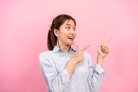 Joven mujer asiática con camisa de manga larga y el uso de las manos con dos precursores para señalar la publicidad en el espacio de copia aislado sobre fondo rosa.