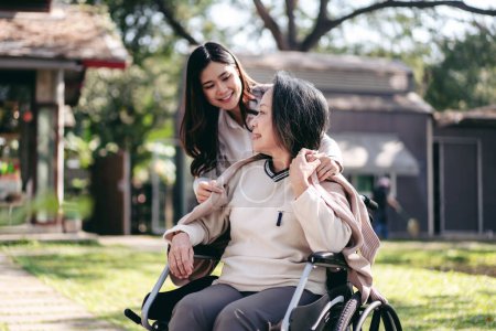 Senior on wheelchair and daughter family concept, Young asian woman blanket disabled mother on wheelchair while senior woman and daughter talking and relaxation together with enjoying in garden.