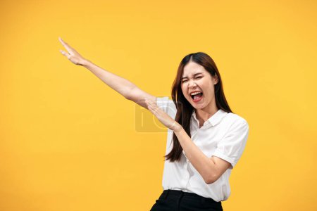 Téléchargez les photos : Jeune femme asiatique portant chemise blanche à manches courtes et levant les mains pour crier de joie après avoir travaillé avec succès isolé sur fond jaune. - en image libre de droit