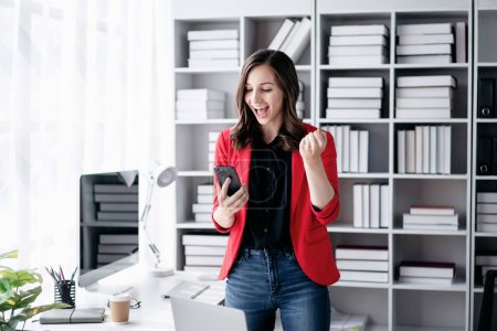 Photo for Accounting business concept, Accountant woman reads good news on smartphone with excited and raising fist to celebrate achievement while working about investment with business planning finance. - Royalty Free Image