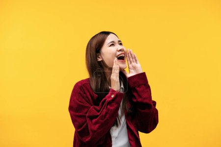 Photo for Young asian woman wearing red jacket and putting her hands near mouth to shouting loudly isolated over yellow background. - Royalty Free Image