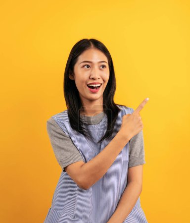 Photo for Young asian woman in casual clothes raising finger up to pointing advertisement something and open mouth with excited face isolated over yellow background. - Royalty Free Image