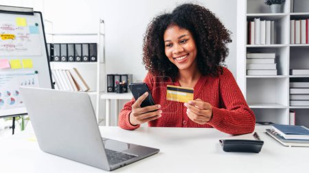 Photo for A woman is smiling while using her cell phone to pay for something. She is holding a credit card in her hand - Royalty Free Image