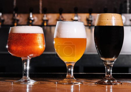 Foto de Diferentes tipos de cerveza artesanal en vasos en la mesa en el interior del pub a la luz del día - Imagen libre de derechos