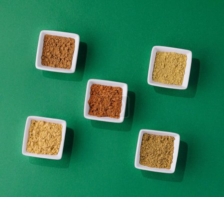 Various Indian Spices in Small White Bowls on green background