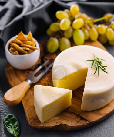 Round cheese on a wooden board and green grapes