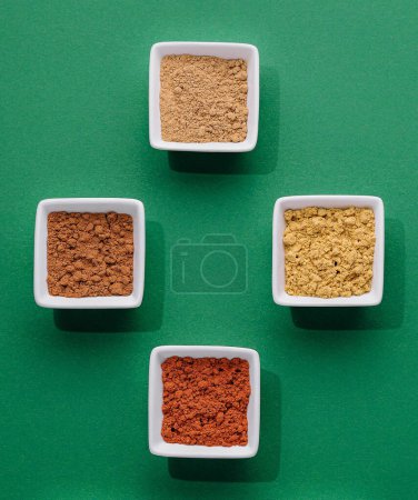 Various Indian Spices in Small White Bowls on Green Background