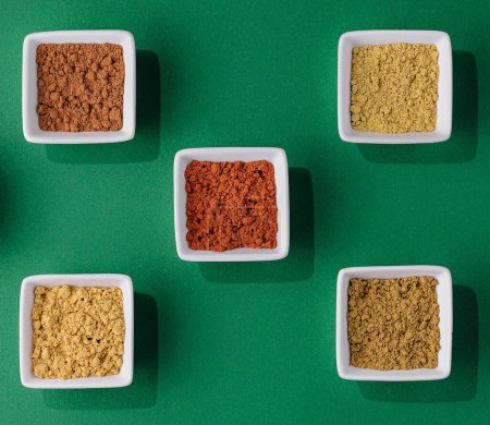 Various Indian Spices in Small White Bowls on Green Background
