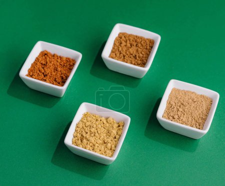Various Indian Spices in Small White Bowls on green background