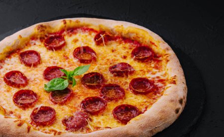 Pepperoni-Pizza mit Basilikum und Parmesan auf schwarzem Steinteller
