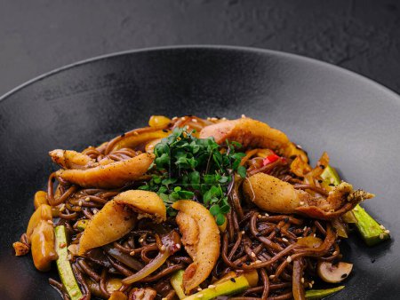 Chinese fried buckwheat pasta with meat on black plate