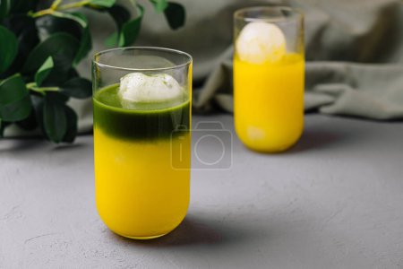 Lebendiger grüner Matcha schwebt neben einem Glas frischem Mangosaft auf schickem grauen Hintergrund