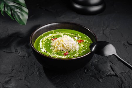 Bowl of vibrant green spinach soup topped with grated cheese, presented elegantly on a dark surface