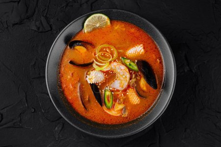 Top view of a bowl of hot and spicy seafood soup with various shellfish, garnished with lime