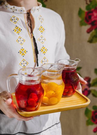 Photo for Person presents three pitchers of refreshing fruit-infused water on a wooden tray - Royalty Free Image
