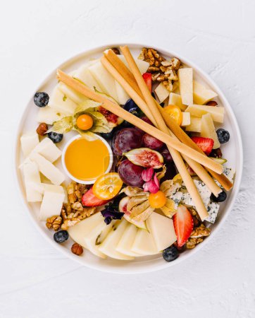Elegant cheese board featuring a variety of cheeses, fresh fruits, nuts and honey, arranged on a white surface