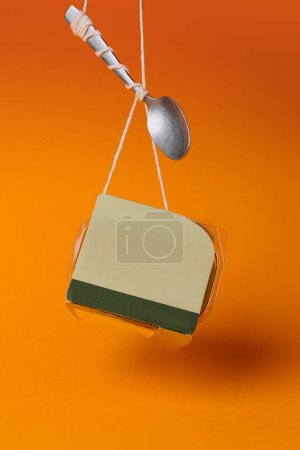 Téléchargez les photos : Image conceptuelle de nature morte du petit déjeuner à emporter et de la cuillère suspendus sur un fond orange vif - en image libre de droit