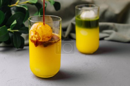 Lebendiges Orangensorbet, das in ein Glas Saft vor schickem grauen Hintergrund gegossen wird