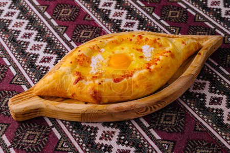 Adjarian khachapuri, a georgian cheese bread, with egg yolk on a rustic patterned tablecloth