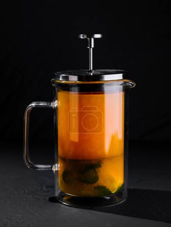 Elegant french press containing vibrant herbal tea, showcased on a dark background