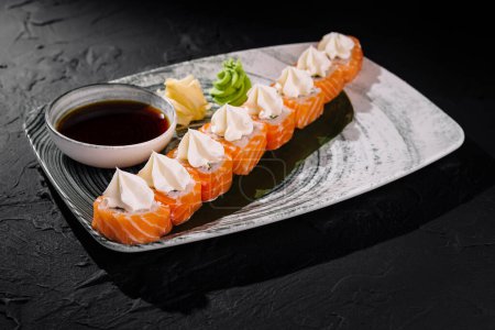 Eleganckie bułki sushi z dodatkiem sera śmietankowego, podawane z sosem sojowym, wasabi i imbirem na szykownym talerzu