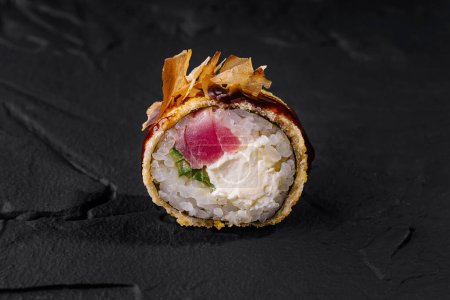 Nahaufnahme einer exquisiten Sushi-Rolle mit frischem Thunfisch und knuspriger Garnitur vor einem texturierten Schiefer-Hintergrund