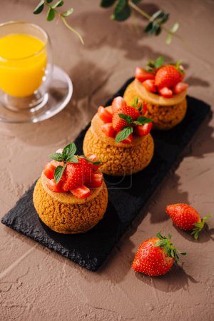 Gourmet tartlets topped with ripe strawberries and mint leaves, served with a glass of orange juice