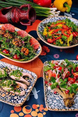 Vibrant mediterranean cuisine served in decorative bowls on a patterned tablecloth with fresh ingredients in the backdrop