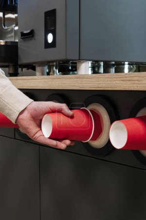 Close-up of a hand pulling a red paper cup from a modern cup dispenser in a cafeteria setting