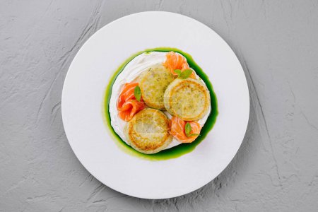 Top view of delicate fish cakes served with a vibrant herb sauce and garnished with salmon pieces