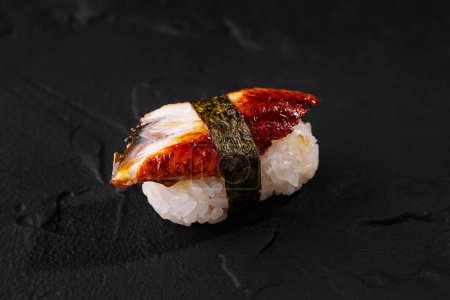 Pojedynczy kawałek pysznego sushi nigiri węgorza prezentowany na teksturowanym czarnym tle łupkowym